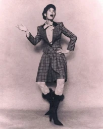 Model Bianca Balti wearing a plaid jacket, matching culottes, beret, and heeled boots against a studio backdrop.