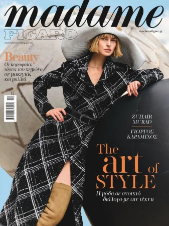 Model in a black plaid coat and wide-brimmed hat posing against a spherical structure for Madame Figaro Greece.