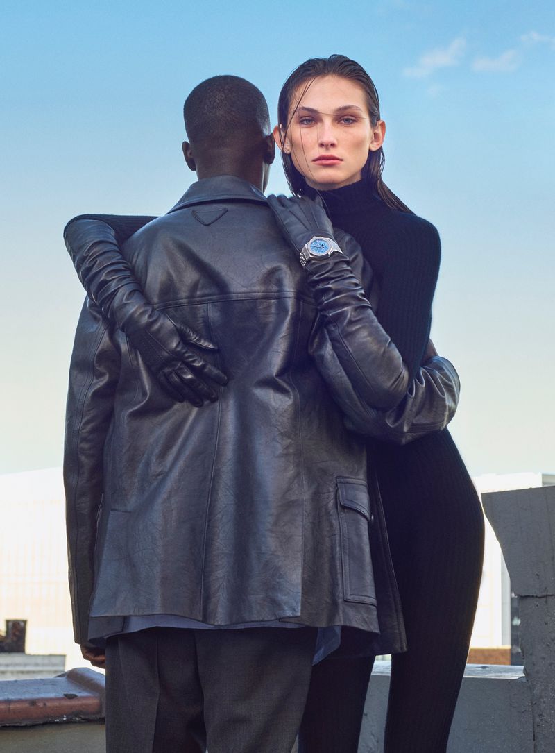 Model Olivia Petersen in long black leather gloves embraces Alpha Dia wearing a black leather jacket against an open sky.