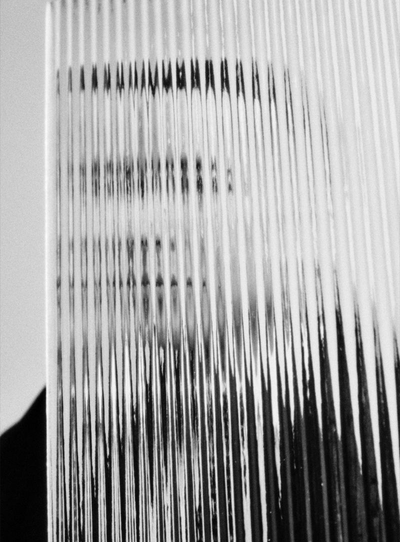 Monochrome abstract portrait through textured glass panel featuring adult's face, obscured features, and diffused lighting.