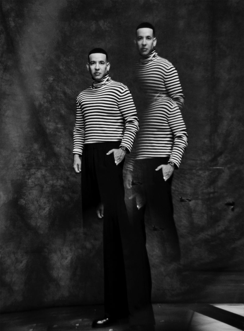 Monochrome portrait of a man in a striped turtleneck and dark trousers, complemented by a blurry, transparent double exposure.