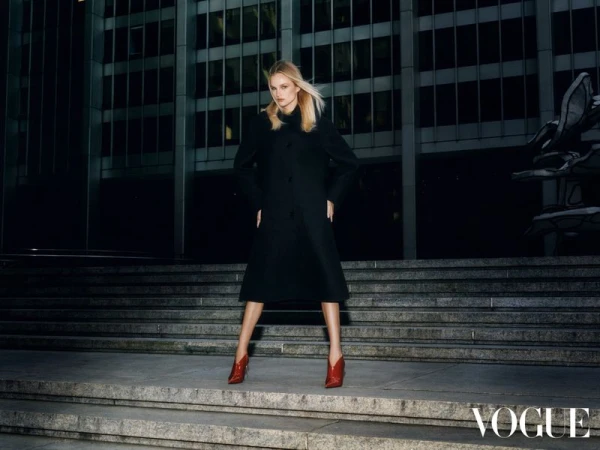 Fashion photography of a blonde woman in a black coat and red shoes posing on stairs in front of a dark building at night.