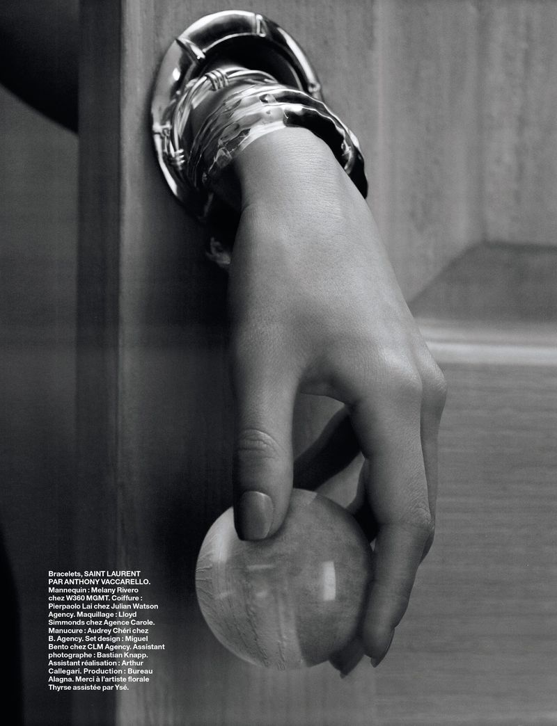 Monochrome close-up of a hand wearing a silver cuff bracelet, grasping a round wooden knob against a wooden door panel.