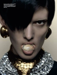 Model Melany Rivero wearing large gold earrings and layered statement necklaces with an oyster shell in her mouth.