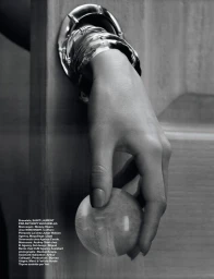 A hand wearing stacked metallic bangles reaches through a circular wall opening, holding a clear glass orb in black and white.