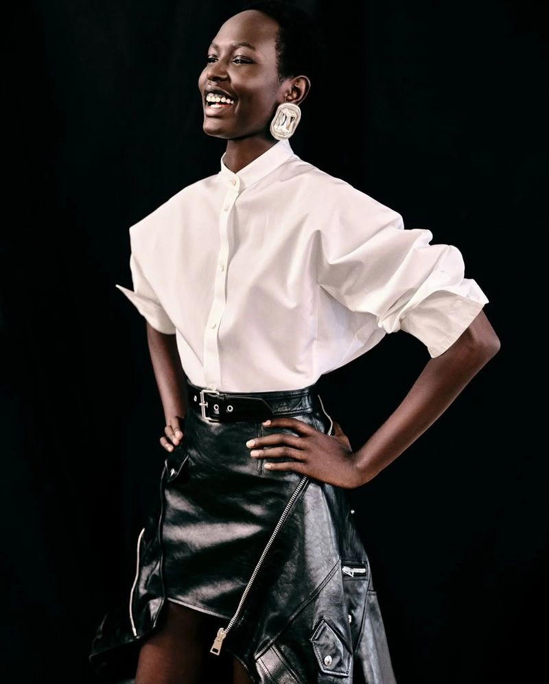 Model wearing a white button-down shirt and black leather skirt against a dark background for Givenchy Spring 2026.