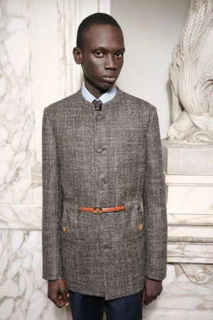 Bukwop Kir wearing a grey tweed mandarin-collar jacket with a thin brown belt for Valentino Pre-Fall 2026.