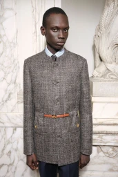 Bukwop Kir wearing a grey tweed mandarin-collar jacket with a thin brown belt for Valentino Pre-Fall 2026.