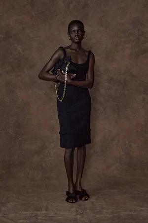 Fashion model Athiec Geng wearing a black knee-length dress and holding a chain-strap bag against a mottled brown backdrop.