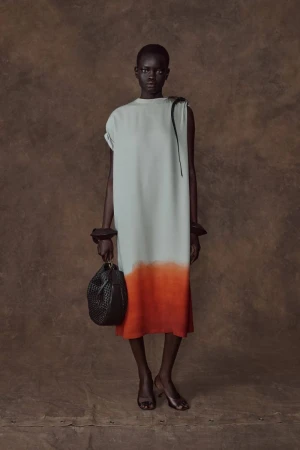 Model Athiec Geng posing in an ivory and orange ombré shift dress with a black handbag against a brown textured backdrop.