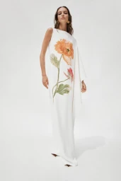 Model posing in a long white asymmetric floral cape dress against a seamless white studio background.
