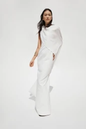 Model Cai Guannan wearing an asymmetric draped white floor-length gown with a gold arm cuff against a white studio background.