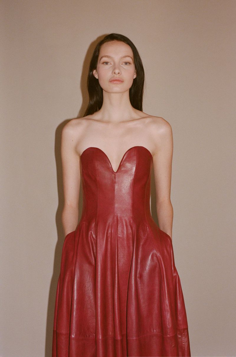 Model wearing a strapless red leather dress against a plain neutral backdrop in a fashion lookbook image