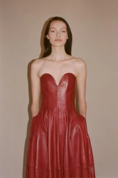 Model wearing a strapless red leather dress against a plain neutral backdrop in a fashion lookbook image