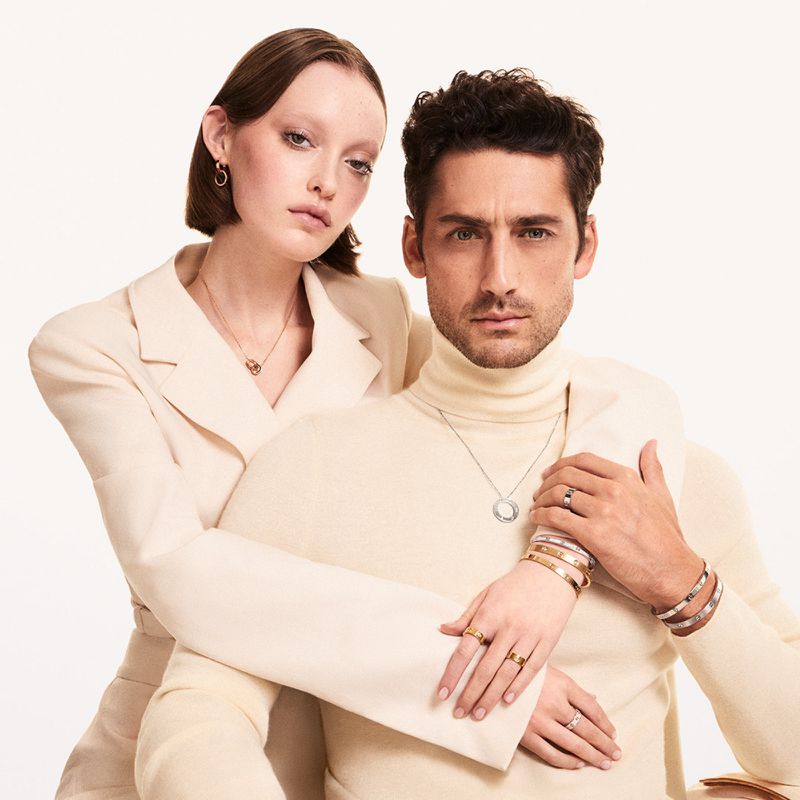 Fashion shot of an adult man and woman wearing coordinated clothing and jewelry in a bright studio. Rings, necklaces, bracelets are visible.