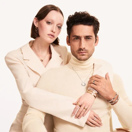 Fashion shot of an adult man and woman wearing coordinated clothing and jewelry in a bright studio. Rings, necklaces, bracelets are visible.