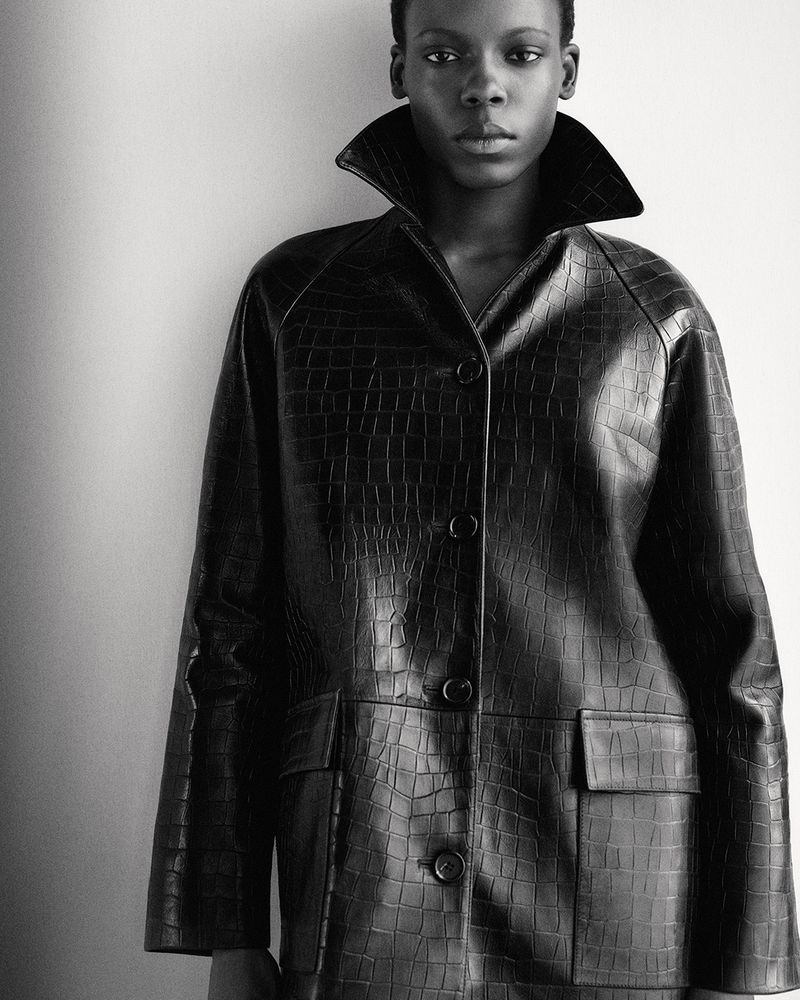 Black and white portrait of a woman in a textured black coat with a wide collar, against a neutral background, fashion editorial.