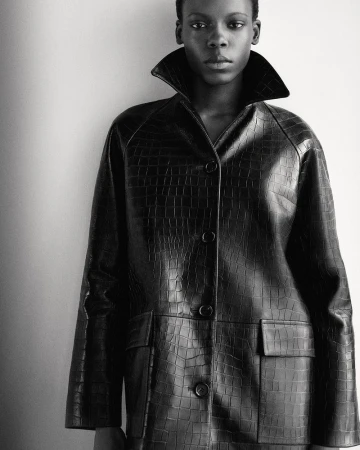 Black and white portrait of a woman in a textured black coat with a wide collar, against a neutral background, fashion editorial.