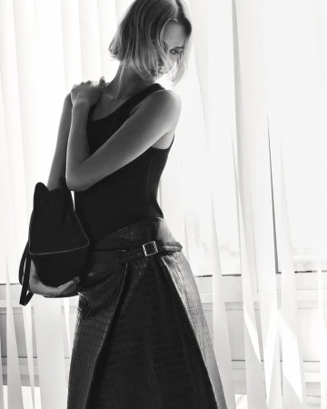 Model Quinn Mora holding a dark bag wearing a black tank top and belted embossed wrap skirt for COS Pre-Fall 25.