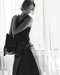 Model Quinn Mora holding a dark bag wearing a black tank top and belted embossed wrap skirt for COS Pre-Fall 25.