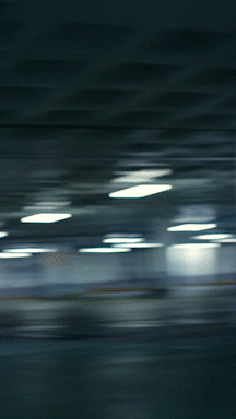 Motion blur of ceiling lights and an orange horizontal line in an indoor parking garage with a grey ceiling and walls.