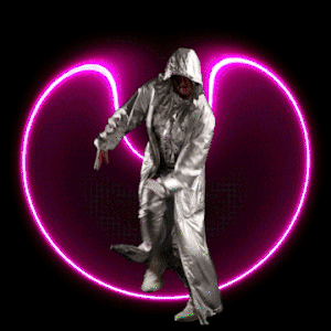 Person in shiny silver hooded suit dancing in front of a glowing pink heart against a dark background, captured with a medium shot.