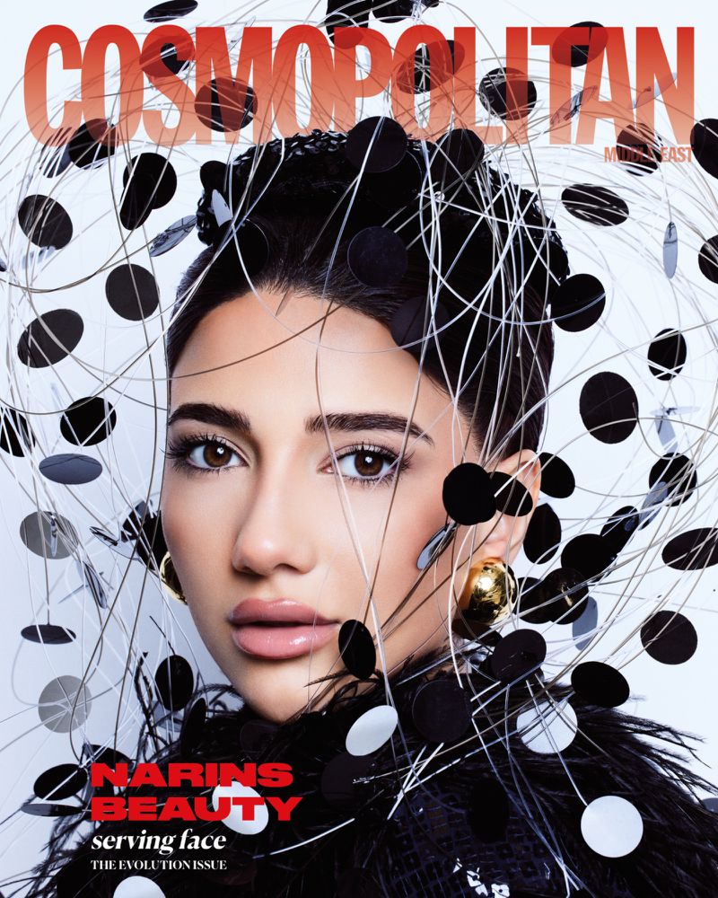Cosmopolitan cover featuring a woman with dark hair and gold earrings surrounded by black and silver artistic designs and black feathered collar.