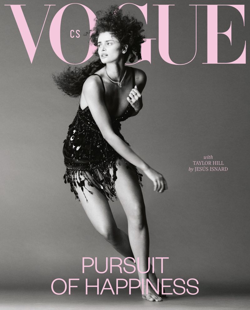 Vogue cover featuring Taylor Hill, wearing a black fringe dress and posing against a grey background, with pink Vogue masthead.