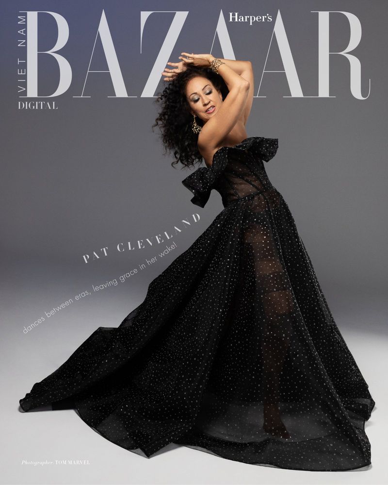 Pat Cleveland poses in a black strapless dress with flowing skirt, in a fashion editorial against a grey backdrop for Harper's Bazaar.