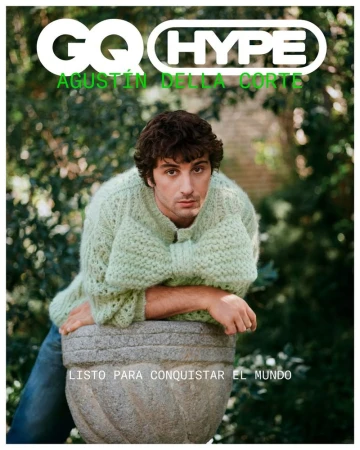 Magazine cover featuring Agustin Della Corte. He is wearing a light green sweater and leans against a stone planter outdoors in a garden setting.