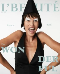 Model Bianca Balti wearing a black halter top and cap with white eyebrows on a white seamless background for L'Beaute Magazine.