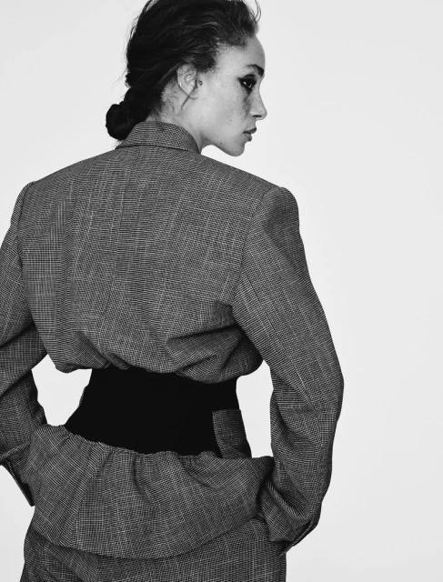 Monochrome studio shot of a stylish adult woman wearing a gray suit with a black waist cincher, looking away from the camera.