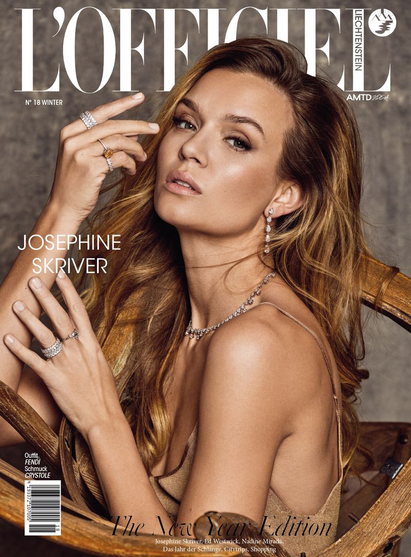 Josephine Skriver poses with jewelry for a L'Officiel Lichtenstein magazine cover, inside a wooden chair in a medium shot.