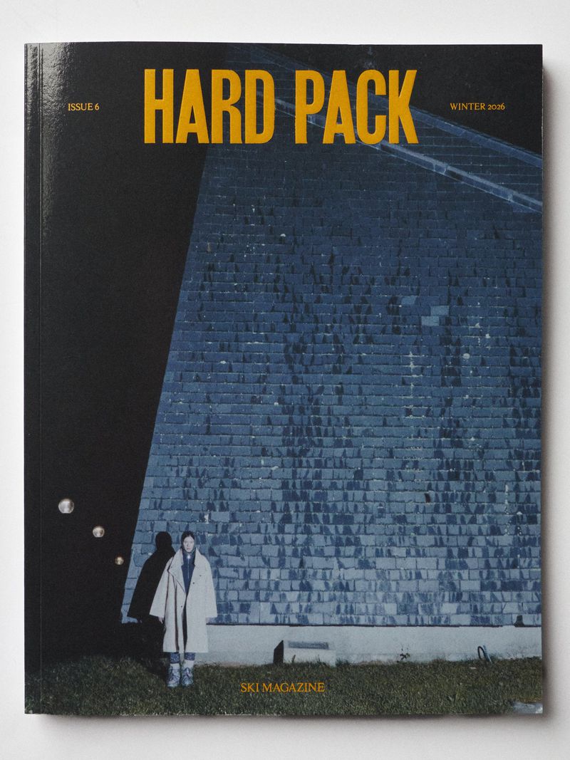 Cover of Hard Pack ski magazine featuring a person in a coat standing in front of a large brick structure at night.