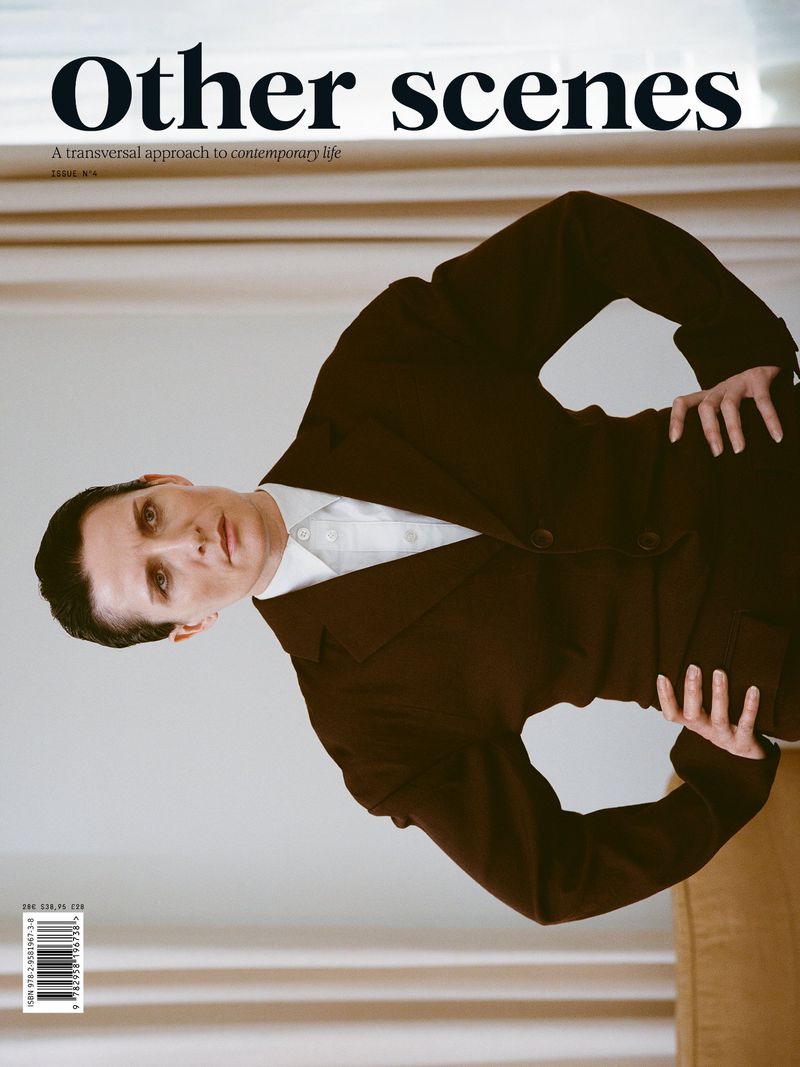 Magazine cover featuring an adult in a dark suit against a neutral backdrop, showcasing fashion and editorial style.