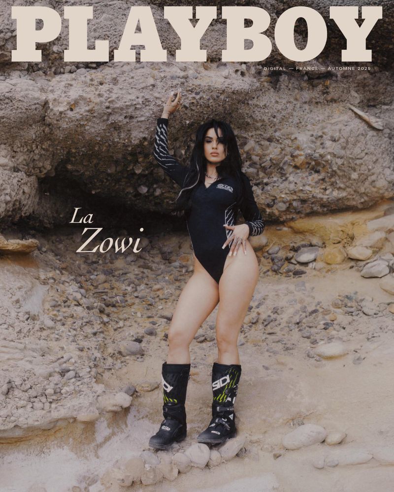 Playboy cover with La Zowi in a black bodysuit and moto boots, posing against a rock formation; sandy outdoor setting with natural light.