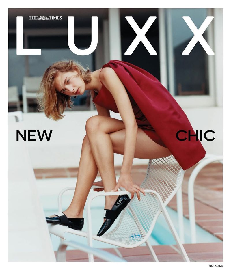 Fashion editorial cover of The Times LUX featuring a fair-skinned model in a red dress and black shoes, posed on a white chair by a pool.