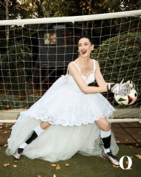 Erin O'Connor in white lace dress and football boots catching a soccer ball in front of a goal for The Observer Magazine