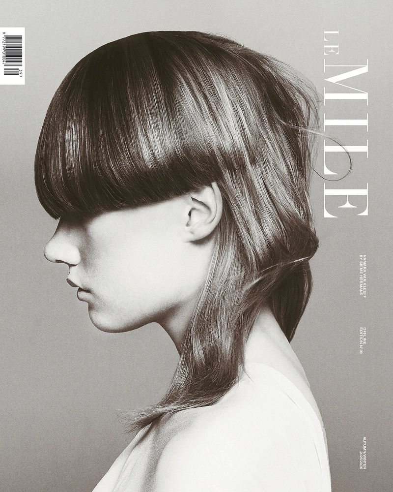 Profile portrait of a model with a bowl cut hairstyle and bangs covering the eyes against a grey background