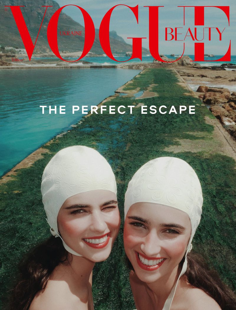 Magazine cover featuring two women with swimming caps smiling against a backdrop of the sea, mountains, and the text 'Vogue Beauty'.