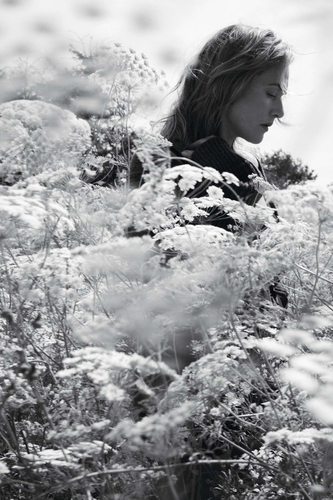 Kate Winslet standing amidst tall wild meadow flowers in a monochrome editorial portrait.