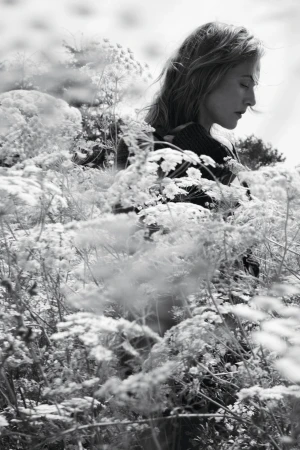 Kate Winslet standing amidst tall wild meadow flowers in a monochrome editorial portrait.