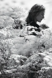 Kate Winslet standing amidst tall wild meadow flowers in a monochrome editorial portrait.