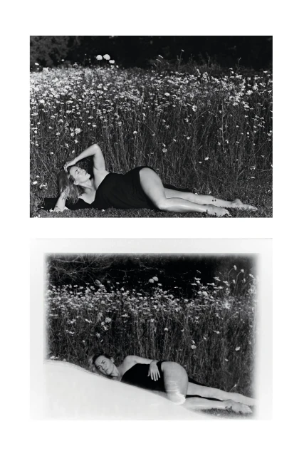 Monochrome outdoor portrait of a reclining adult woman in a black garment amidst a field of daisies with dark woods in the background.