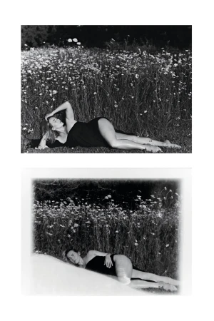 Monochrome outdoor portrait of a reclining adult woman in a black garment amidst a field of daisies with dark woods in the background.