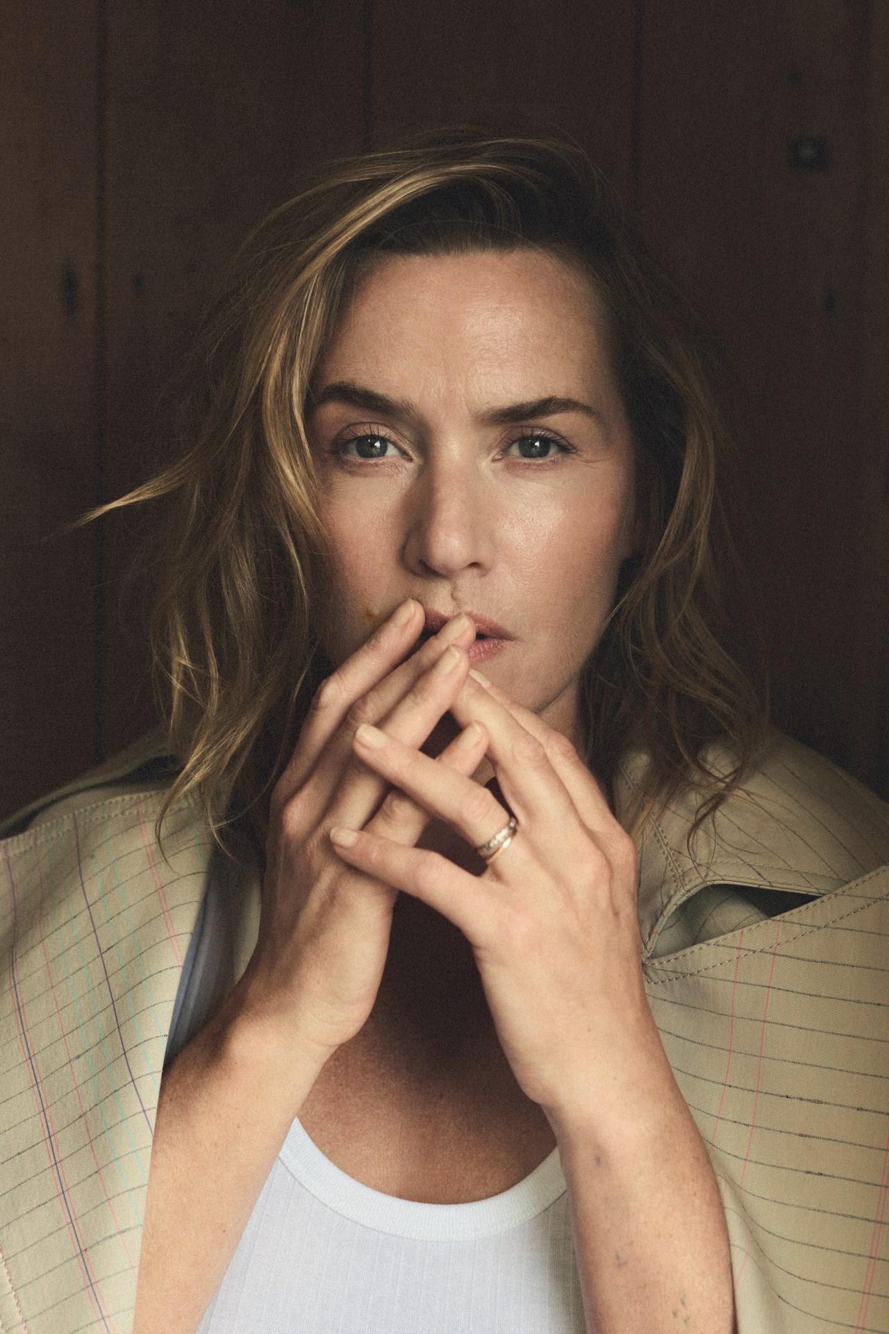 Close-up portrait of a fair-skinned adult female with tousled blonde hair and crossed hands, wearing a white top and striped jacket.