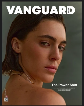 Close-up portrait of a woman with dark slicked-back hair and minimal makeup against a soft muted background for Vanguard Magazine.
