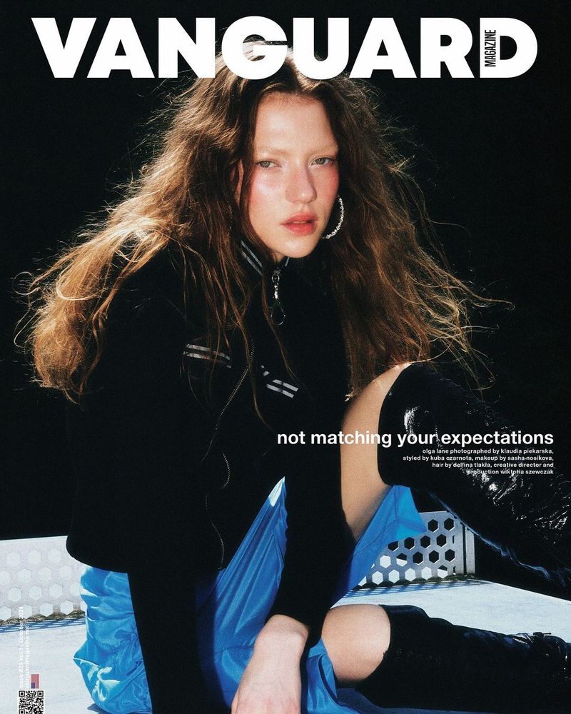 Model wearing black jacket and blue skirt seated outdoors against a dark night sky for Vanguard Magazine cover