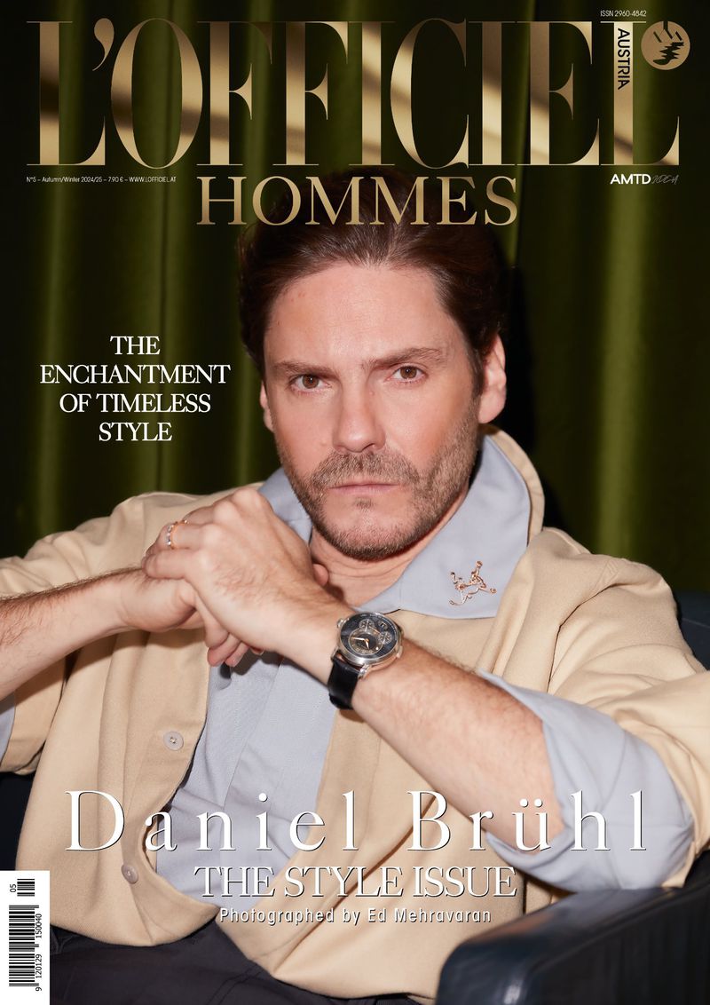 Magazine cover featuring Daniel Brühl in a beige jacket and light blue shirt, posing in front of a green curtain for L'Officiel Hommes.