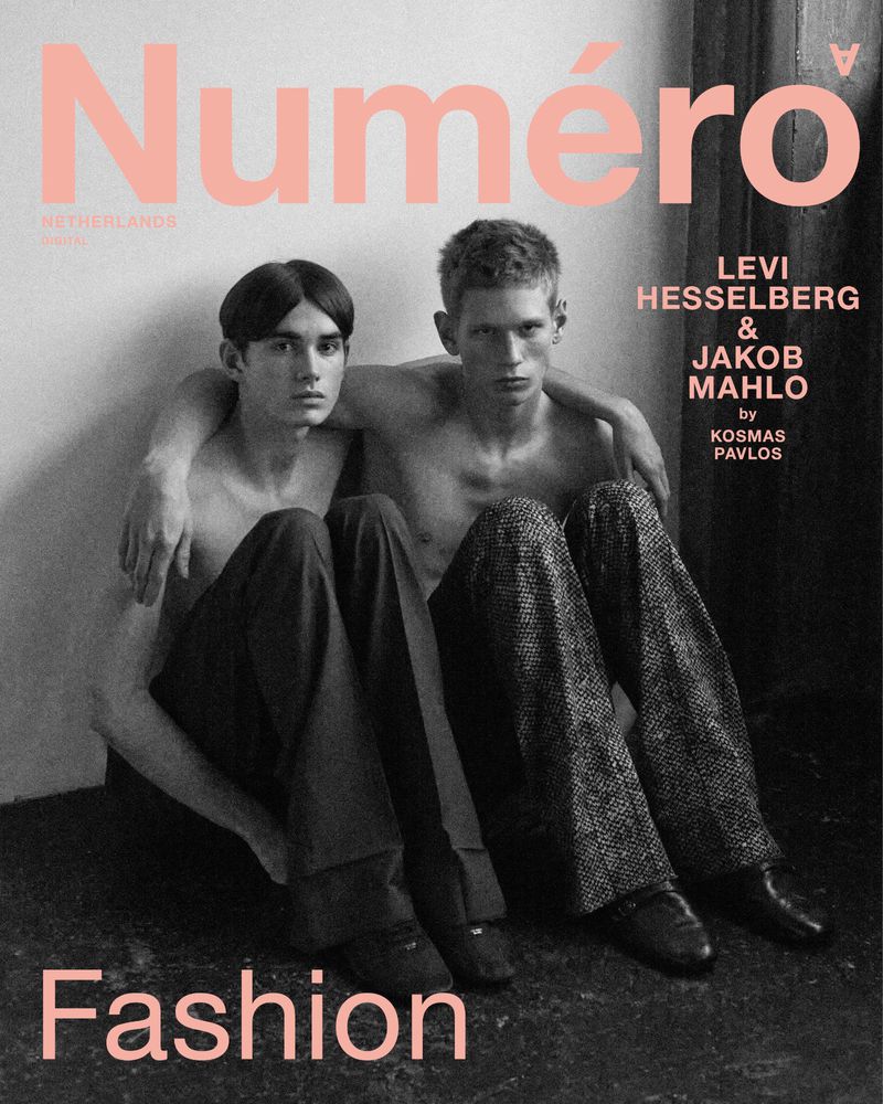 Two shirtless male models sitting closely together on a floor against a plain wall for a digital magazine cover.